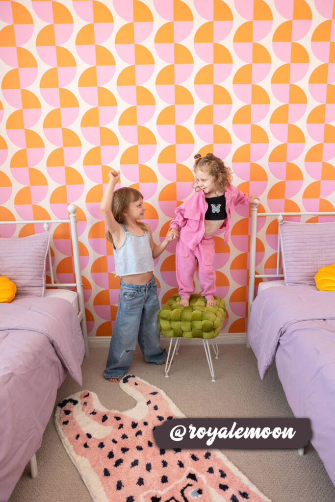 Vibrant pink and orange geometric wallpaper adds a playful and lively atmosphere to a shared kids' bedroom, complementing pastel bedding and a cheerful decor setup