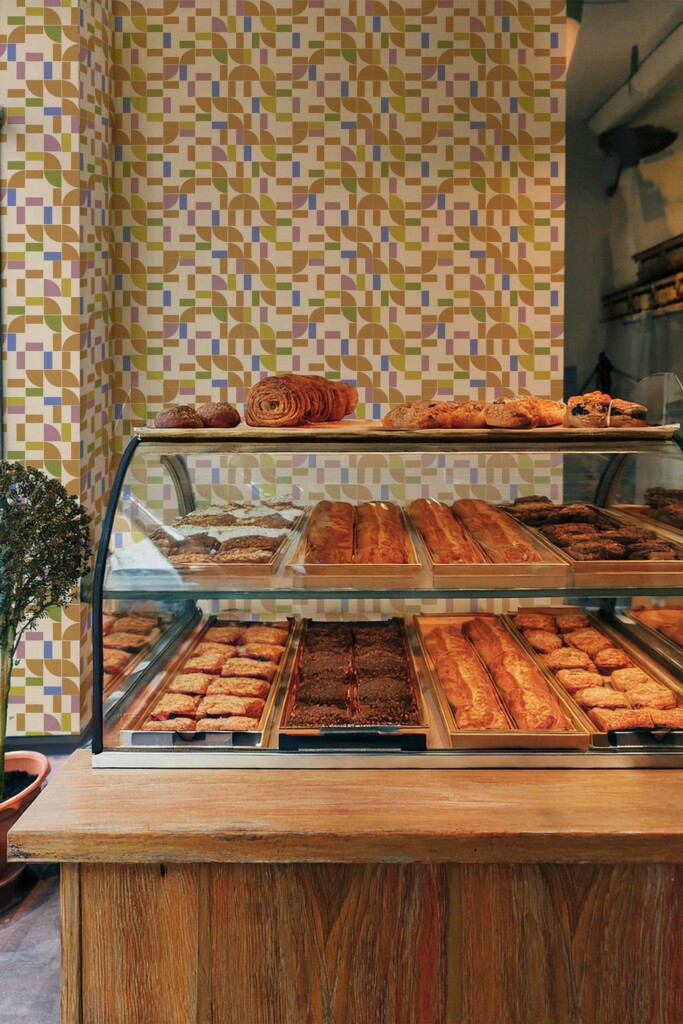 Interior of a bakery with shelves of fresh pastries and Groovy Geometric wallpaper in the background. The multicolored tile pattern brings cheerful energy and vintage charm to a modern retail space.