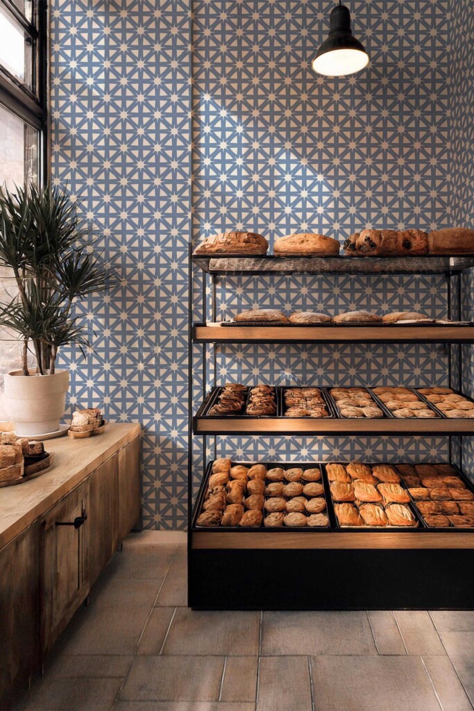 Bakery wall decorated with French Country Starburst wallpaper, showcasing a soft blue hand-drawn tile pattern with beige stars. Wooden shelving filled with pastries highlights the wallpaper’s retro café appeal. Fancy Walls peel and stick or non-pasted wallpaper enhances the cozy bakery setting.