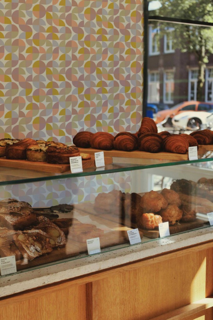 Artisan bakery featuring a pastry case with fresh goods, backed by Bakery Retro Colorful wallpaper. The light beige background and multicolored tiles add depth and personality to retail walls.