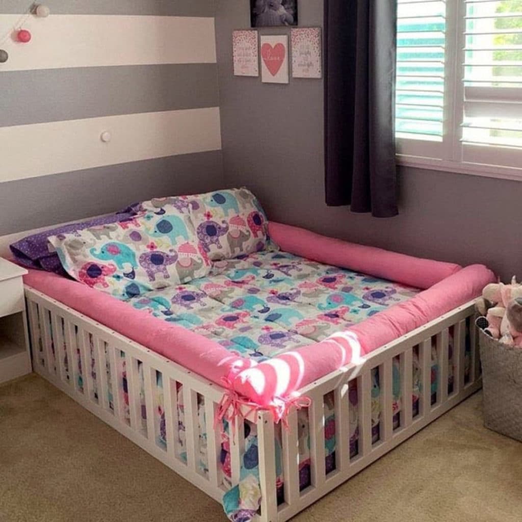 A natural wood toddler bed with a mattress and bedding